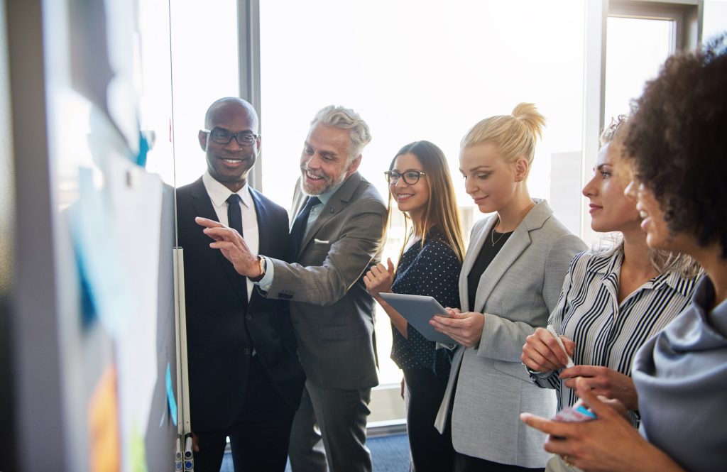 Smiling colleagues strategizing together on a whiteboard in an office